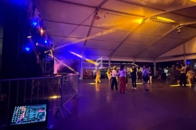 Des personnes dansent sous un chapiteau éclairé par des lumières colorées, avec une table de mixage au premier plan.