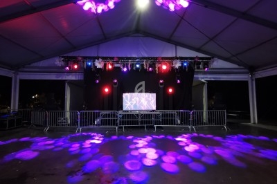 Scène sous chapiteau avec éclairage violet et rose, barrière de sécurité et écran central en arrière-plan.