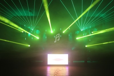 Effets lumineux verts et jaunes avec lasers et écran lumineux sur une scène dans une ambiance enfumée.