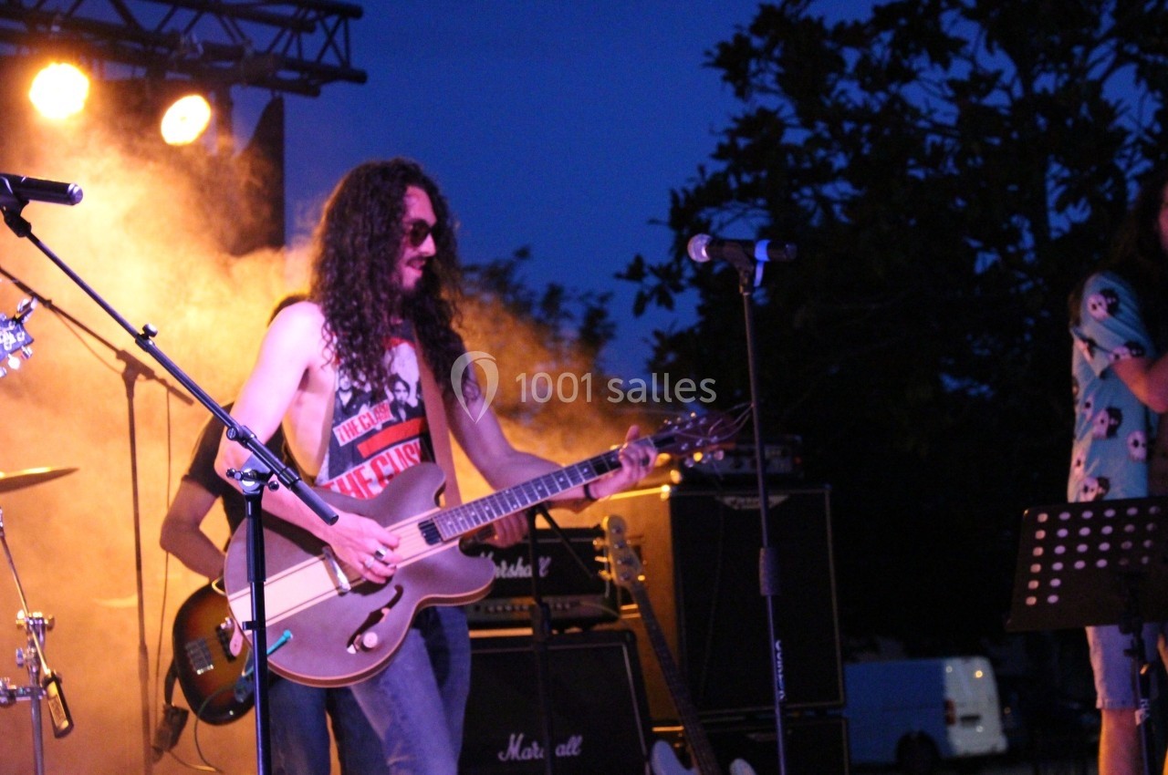 Un musicien joue de la guitare électrique sur une scène extérieure éclairée, entouré de matériel audio.