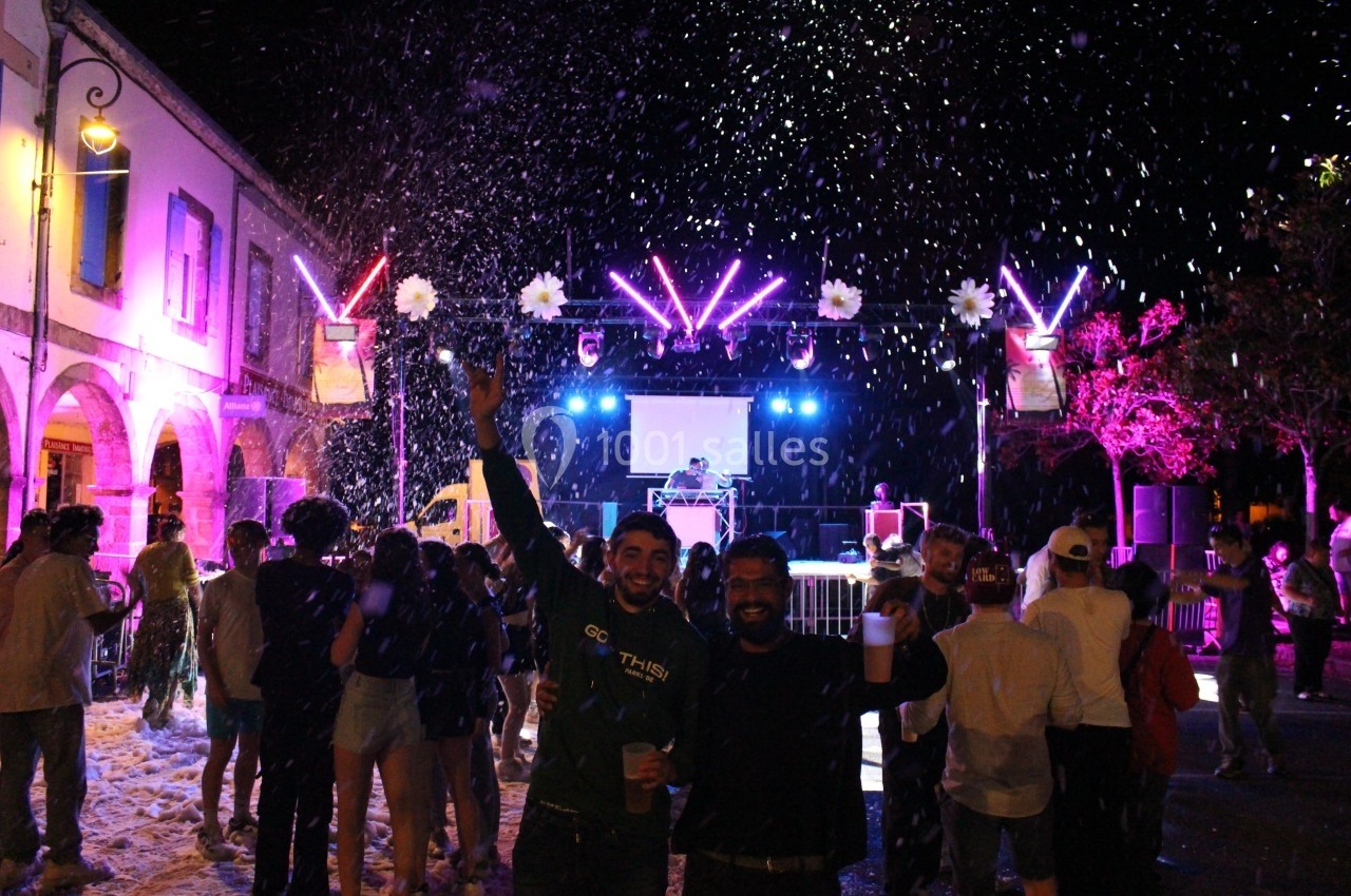Groupe de personnes dansant en soirée extérieure avec lumières colorées et neige artificielle.