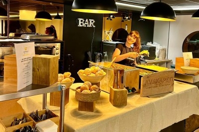 Buffet avec pains, plats variés et une personne servant de la nourriture sous des lampes suspendues.