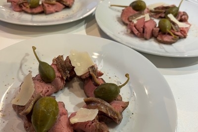Assiettes de carpaccio de bœuf garnies de câpres, anchois et copeaux de parmesan, disposées sur une table.