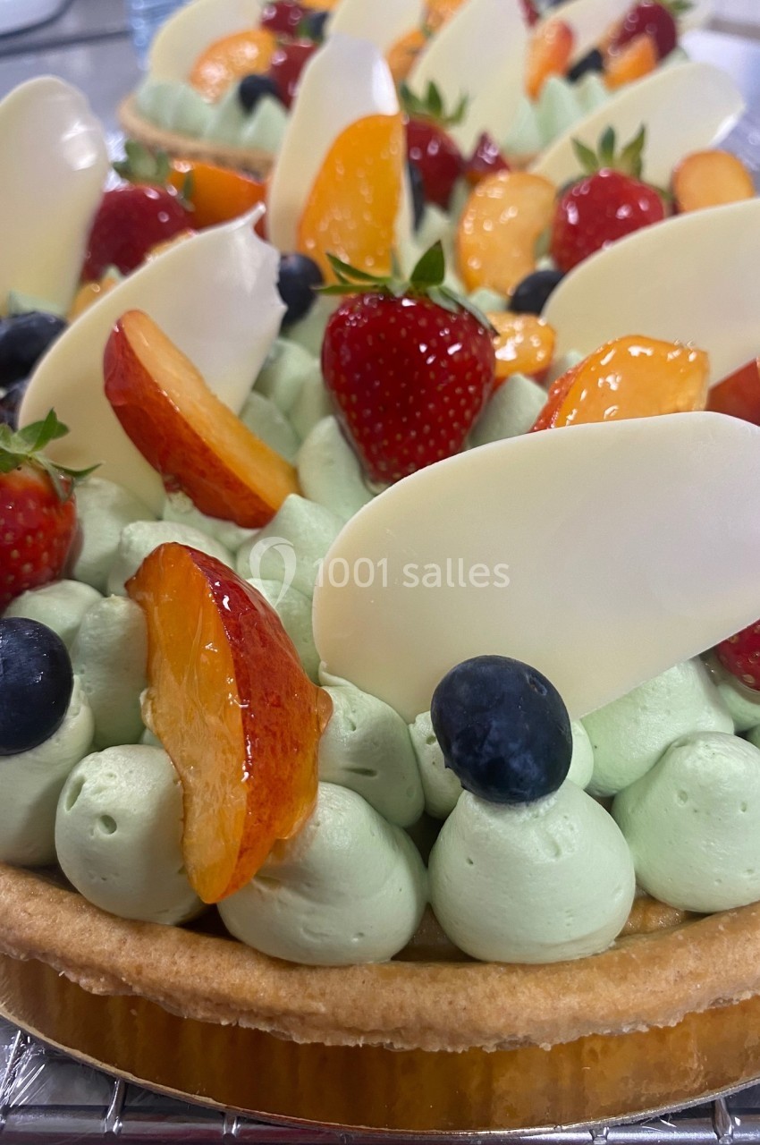 Tarte garnie de crème verte, décorée de fraises, myrtilles, tranches de pêche et éclats de chocolat blanc.