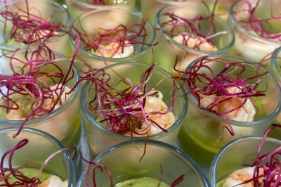 Miniature Traiteur Fréjus (Var) - La Cuisine By Alexandre #7 Salle de réception lumineuse avec tables rondes décorées de fleurs et vaisselle élégante, éclairée par des guirlandes.