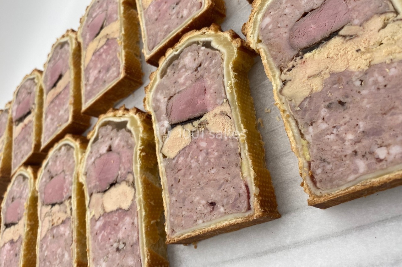 Tranches de pâté en croûte alignées sur une surface blanche, révélant des couches de viande et de foie gras.
