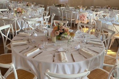 Miniature Traiteur Fréjus (Var) - La Cuisine By Alexandre #25 Salle de réception lumineuse avec tables rondes décorées de fleurs et vaisselle élégante, éclairée par des guirlandes.