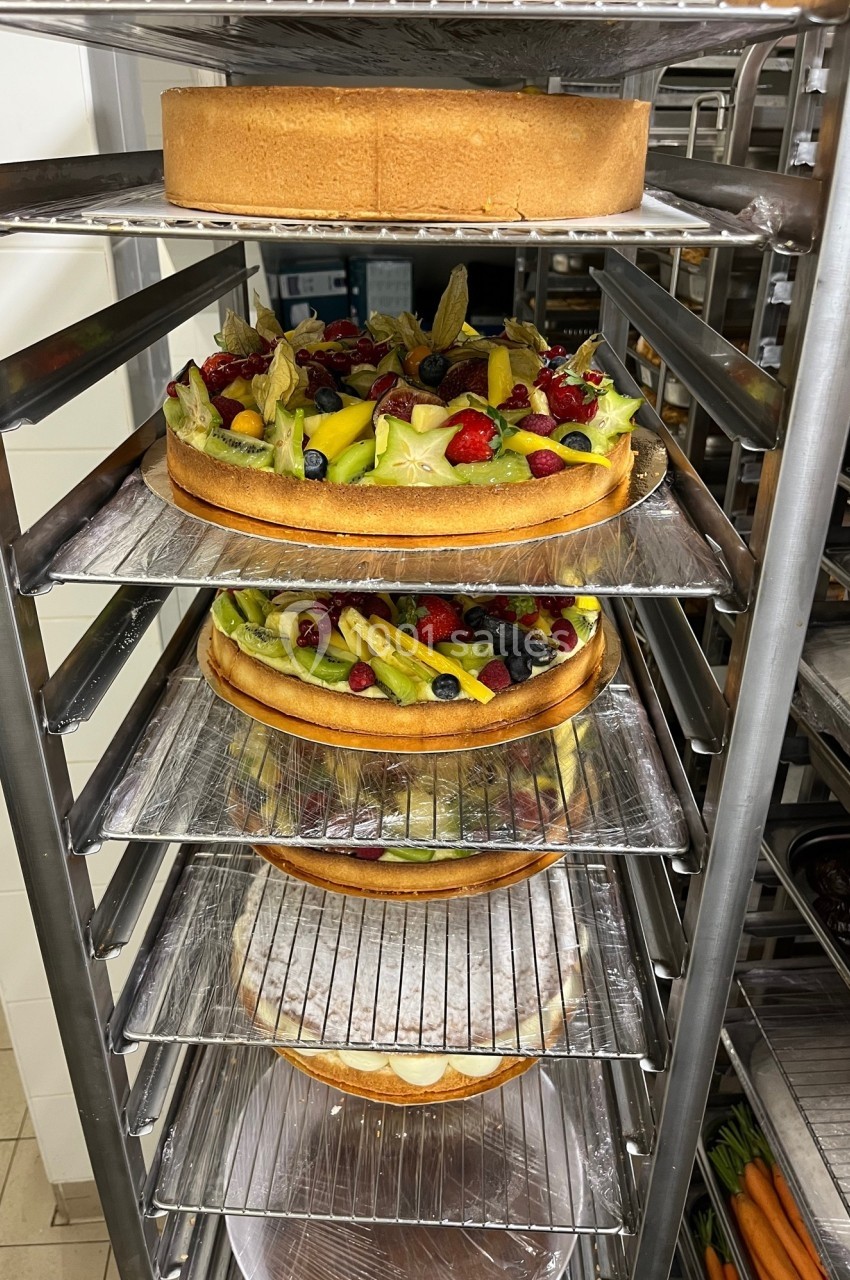 Gâteaux garnis de fruits frais et tartes sur des étagères métalliques dans une cuisine professionnelle.
