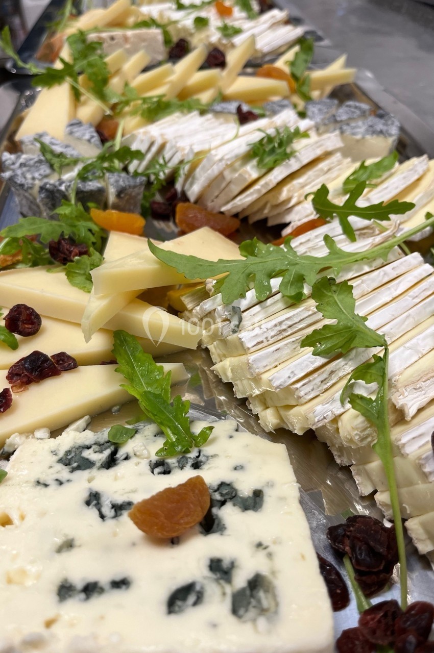 Plateau de fromages variés avec brie, fromage bleu, morceaux de fruits secs et roquette en garniture.