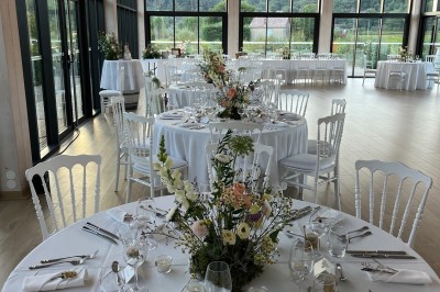 Miniature Traiteur Fréjus (Var) - La Cuisine By Alexandre #40 Salle de réception lumineuse avec tables rondes décorées de fleurs et vaisselle élégante, éclairée par des guirlandes.
