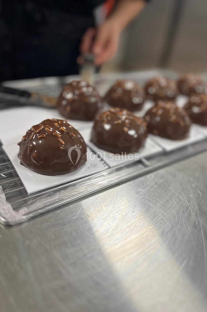 Chocolats enrobés de glaçage brillant disposés sur des feuilles de papier dans une cuisine professionnelle.
