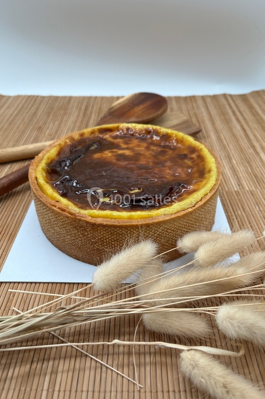 Tarte au flan dorée posée sur un tapis en bambou, entourée de cuillères en bois et de fleurs séchées.