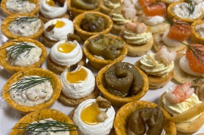 Miniature Traiteur Fréjus (Var) - La Cuisine By Alexandre #5 Salle de réception lumineuse avec tables rondes décorées de fleurs et vaisselle élégante, éclairée par des guirlandes.