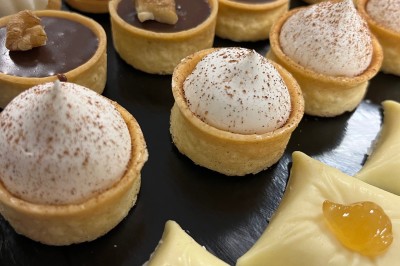 Miniature Traiteur Fréjus (Var) - La Cuisine By Alexandre #21 Salle de réception lumineuse avec tables rondes décorées de fleurs et vaisselle élégante, éclairée par des guirlandes.