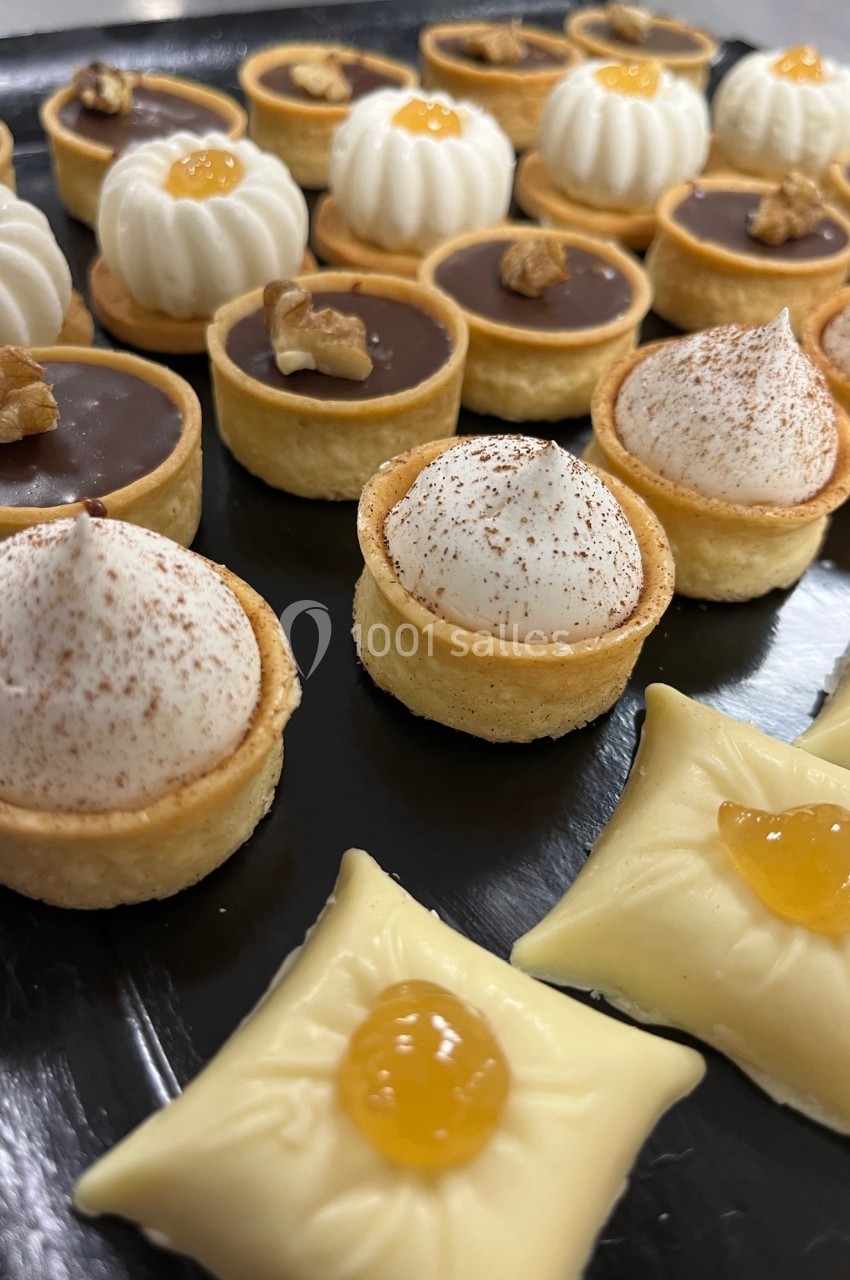 Assortiment de mini-pâtisseries sur un plateau, comprenant tartelettes au chocolat, à la crème et garnies de noix ou de…