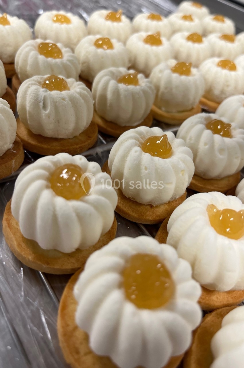 Petits biscuits garnis de crème blanche et d'une touche de confiture jaune, alignés sur une surface transparente.