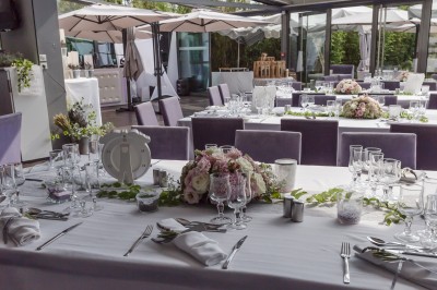 Salle de réception avec tables élégamment dressées, nappes blanches, chaises violettes et décorations florales.