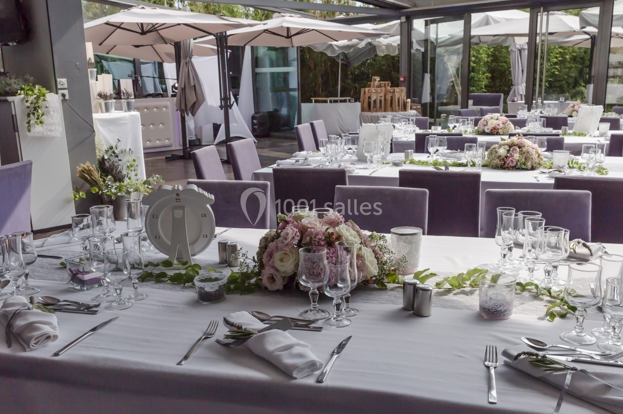 Salle de réception élégante avec tables dressées, décorations florales et grandes baies vitrées donnant sur l'extérieur.