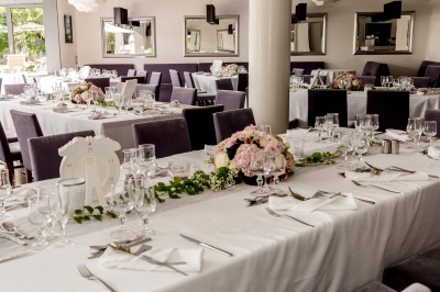 Salle de réception avec tables élégamment dressées, nappes blanches, chaises violettes et décorations florales.