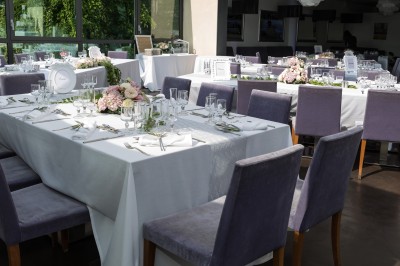 Salle de réception avec tables élégamment dressées, nappes blanches, chaises violettes et décorations florales.