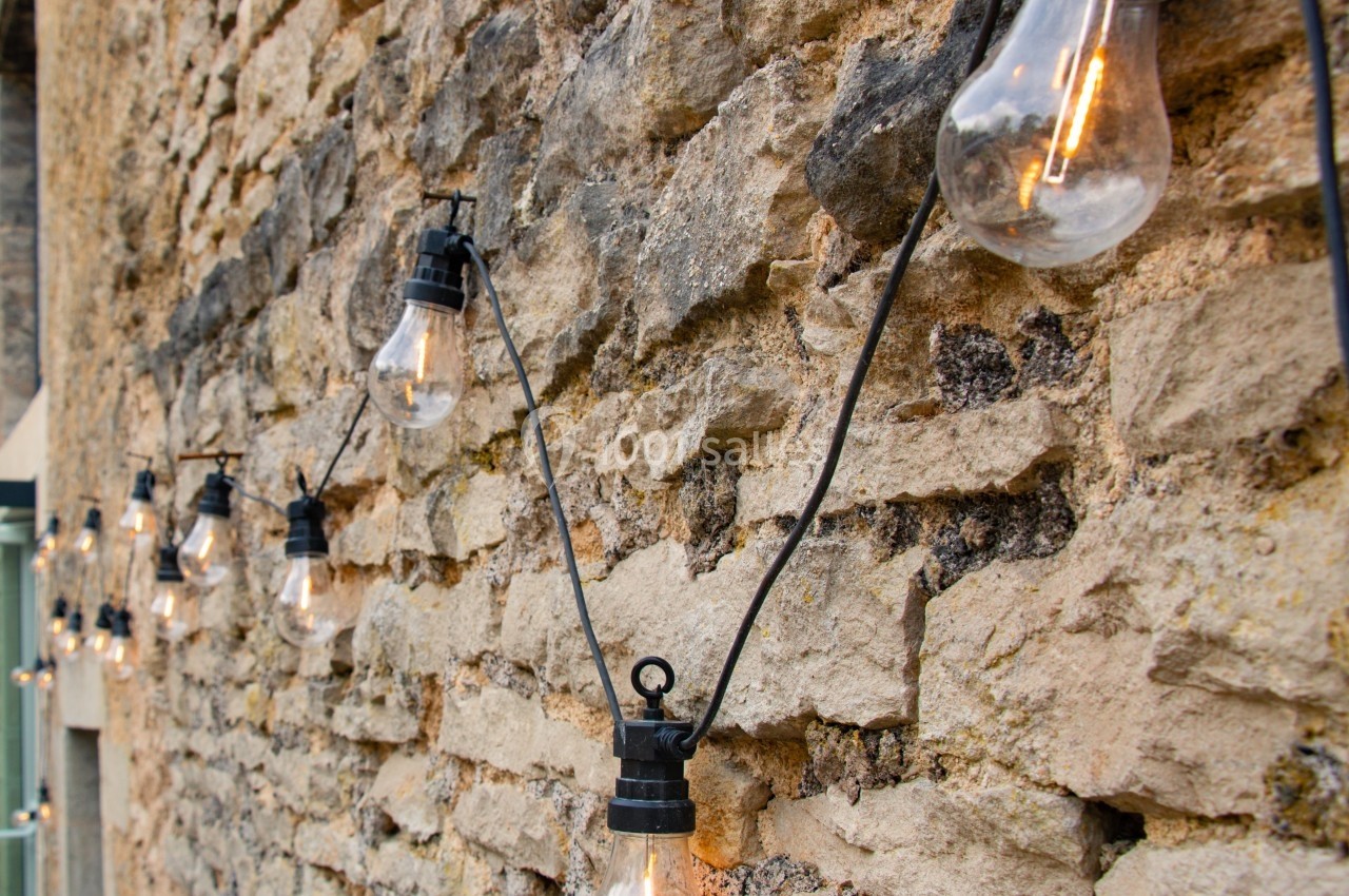 Guirlande d'ampoules suspendue le long d'un mur en pierre, éclairant légèrement l'espace.