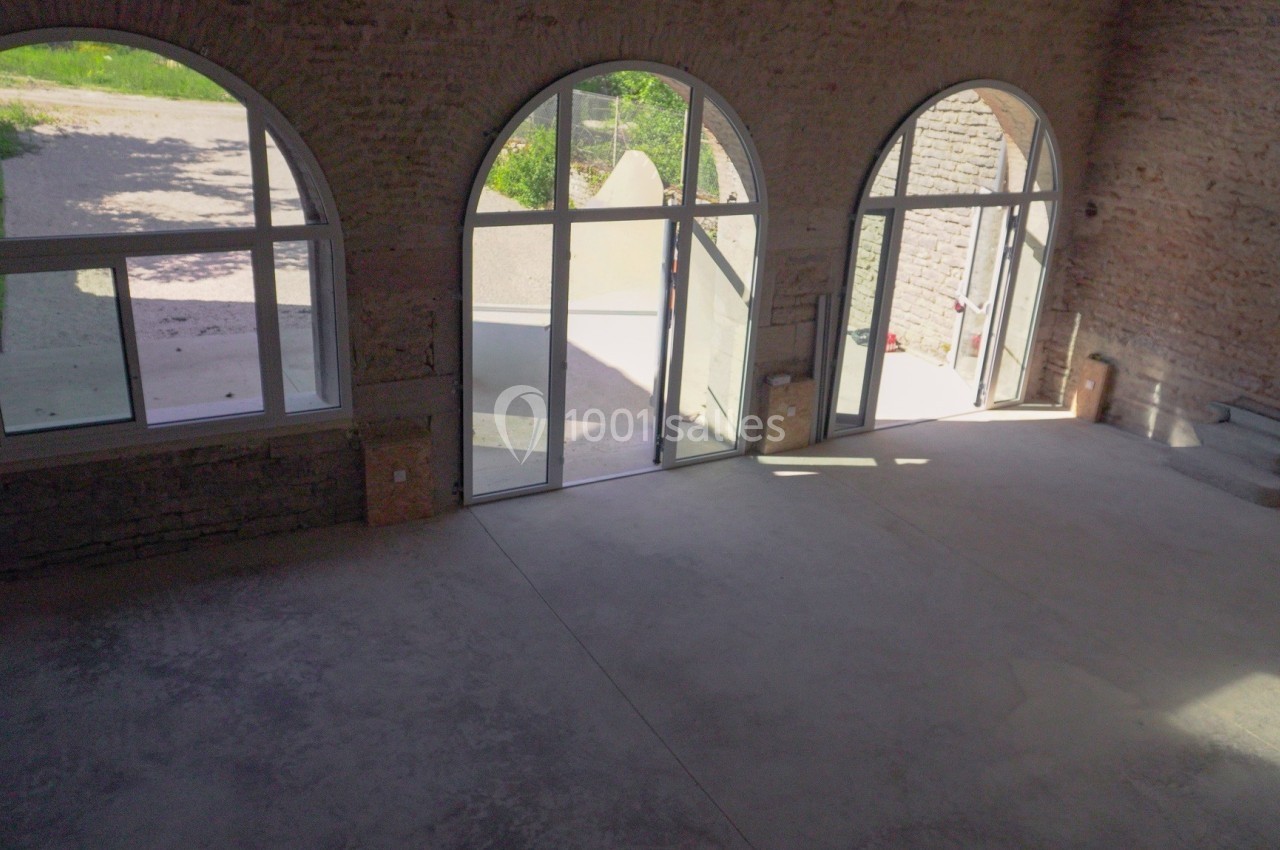 Vue intérieure d'une pièce spacieuse avec de grandes baies vitrées en arc donnant sur un extérieur ensoleillé.