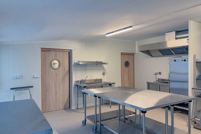 Cuisine professionnelle équipée avec plans de travail en inox, four, hotte d'extraction et portes en bois.