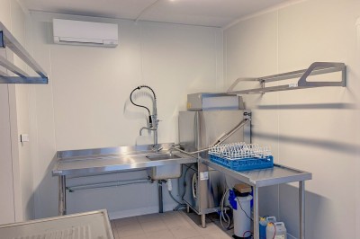 Cuisine professionnelle équipée avec plans de travail en inox, four, hotte d'extraction et portes en bois.