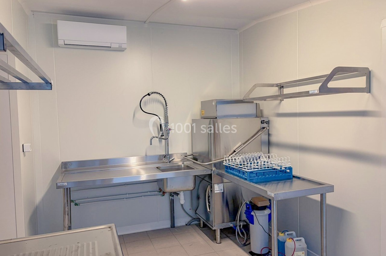Cuisine professionnelle équipée d'un évier inox, d'un lave-vaisselle industriel et de rangements muraux.