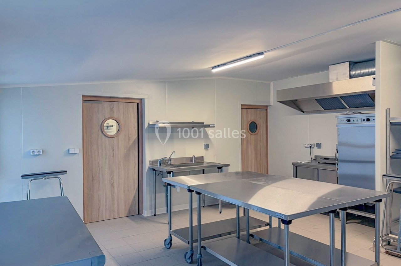 Cuisine professionnelle équipée avec plans de travail en inox, four, hotte d'extraction et portes en bois.