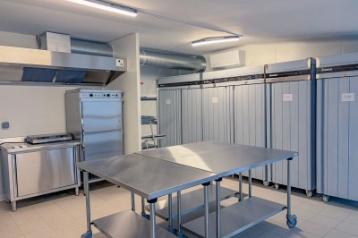 Cuisine professionnelle équipée avec plans de travail en inox, four, hotte d'extraction et portes en bois.