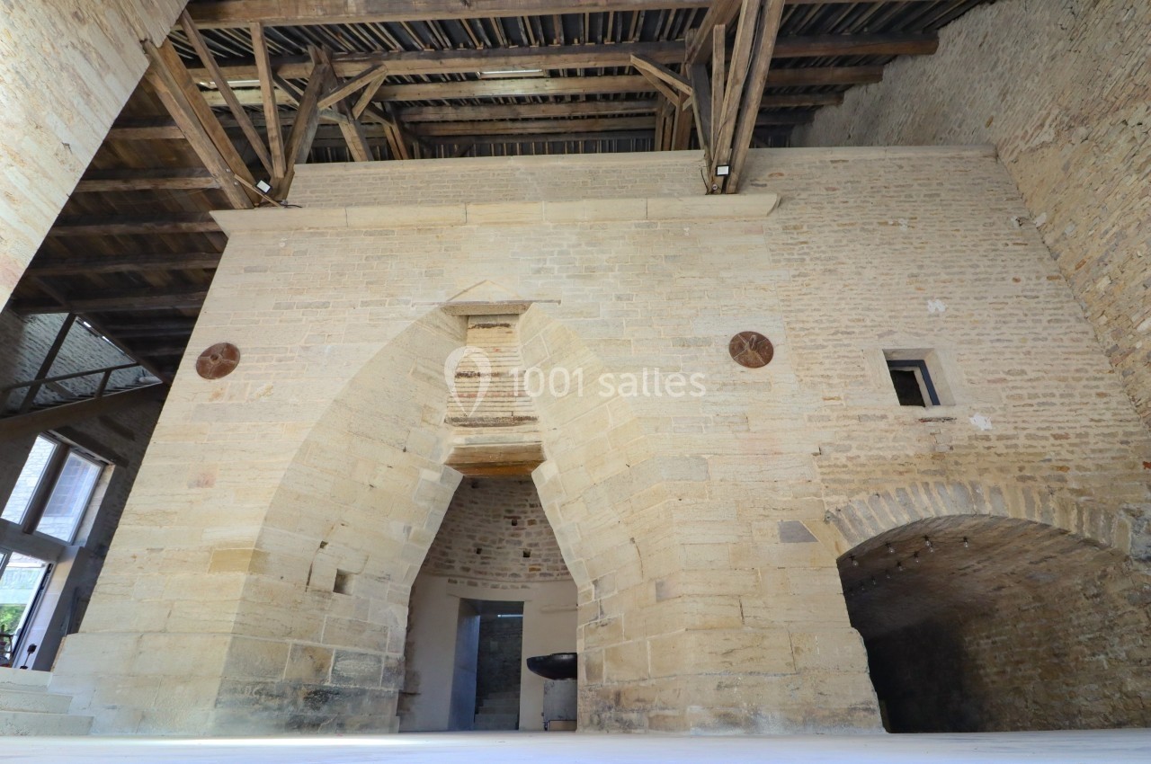 Vue intérieure d'une structure en pierre avec des arches, un plafond en bois et des détails architecturaux anciens.