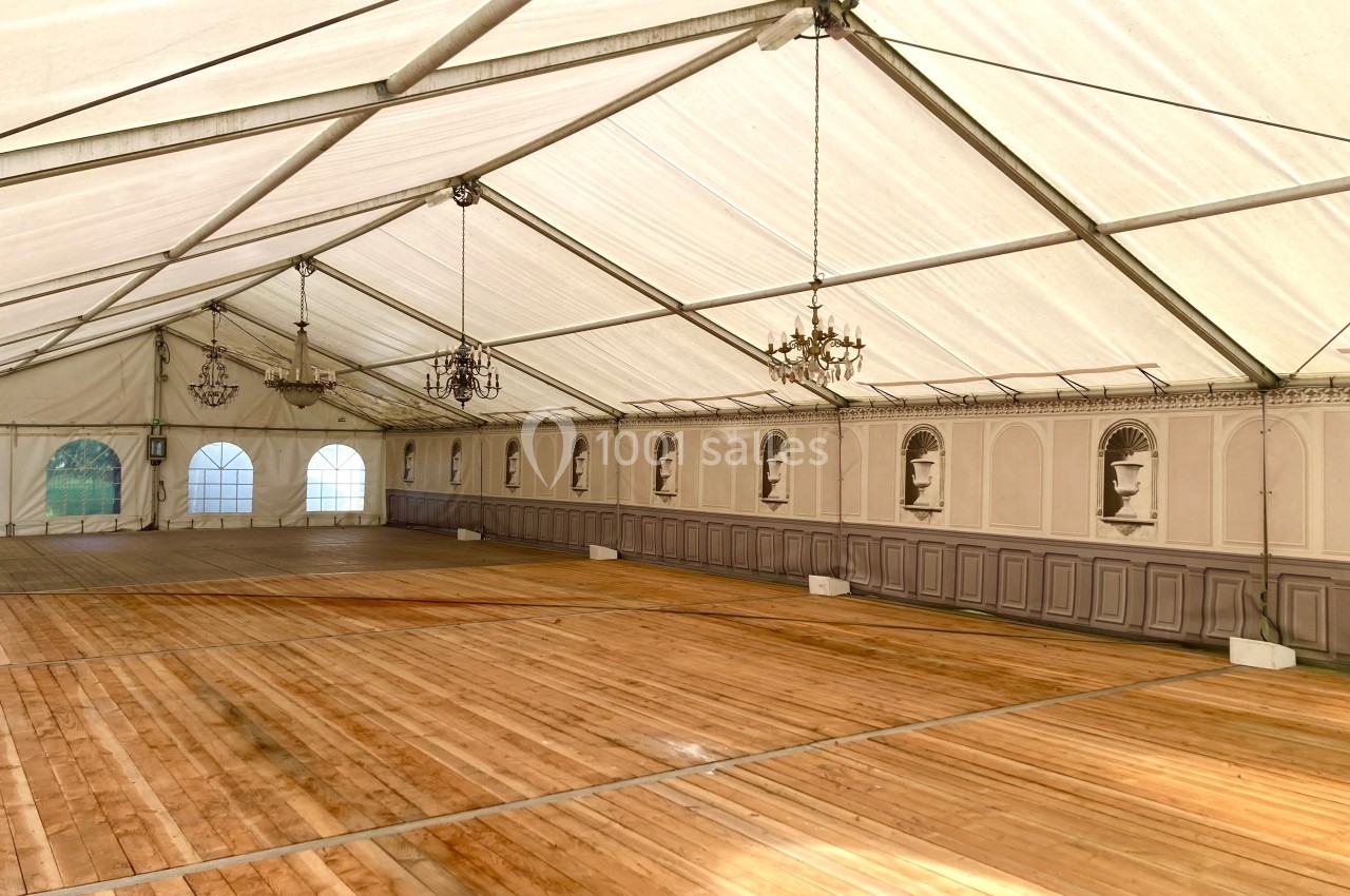 Intérieur d'une grande tente avec plancher en bois, murs décorés de moulures et lustres suspendus.