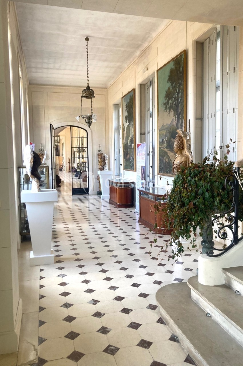 Couloir lumineux avec sol en damier, statues, tableaux accrochés aux murs et escalier en premier plan.
