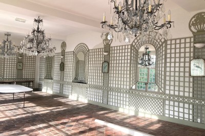 Cuisine ancienne avec une grande table en bois, un sol en pierre, des fenêtres lumineuses et des éléments rustiques.
