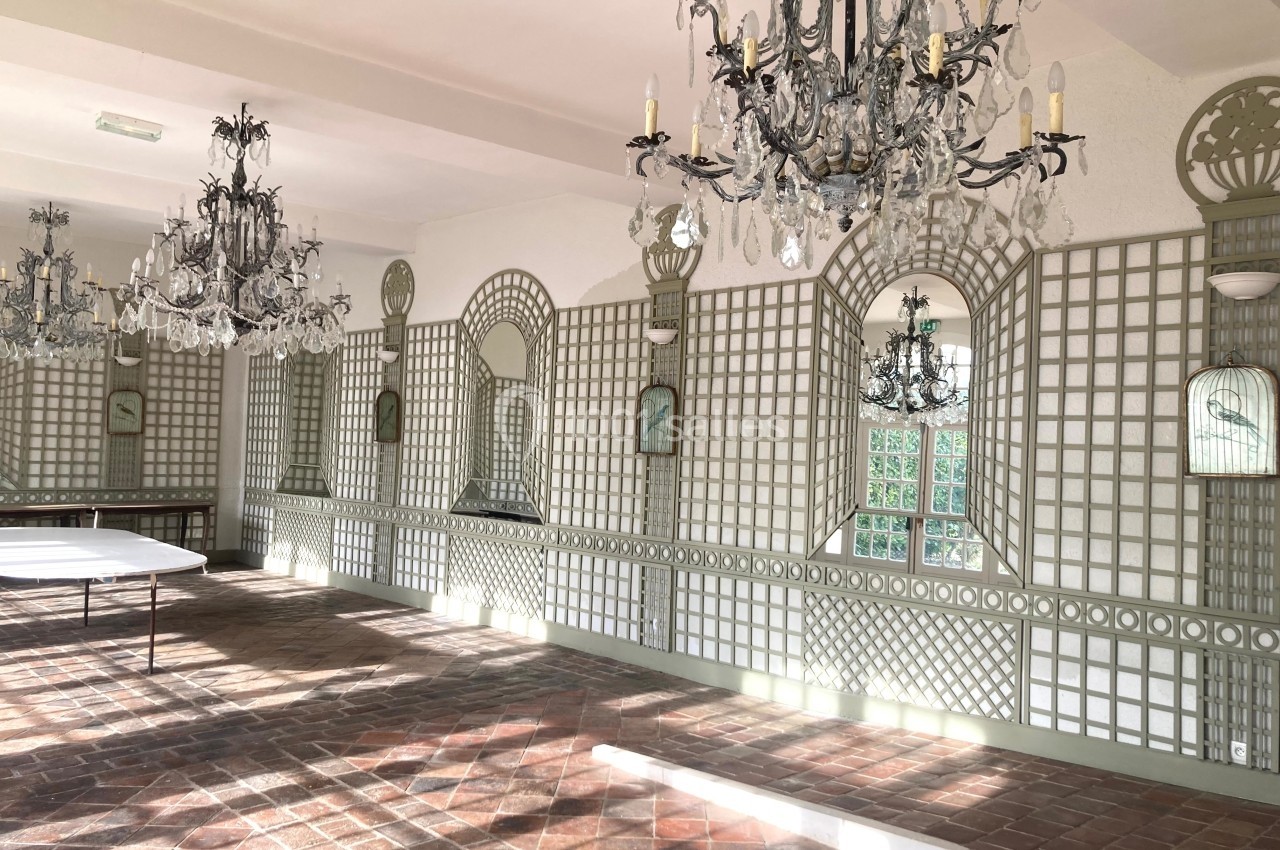 Salle lumineuse avec murs ornés de miroirs et treillis, chandeliers suspendus et sol en carreaux de terre cuite.