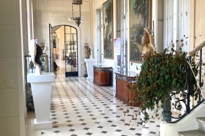 Cuisine ancienne avec une grande table en bois, un sol en pierre, des fenêtres lumineuses et des éléments rustiques.