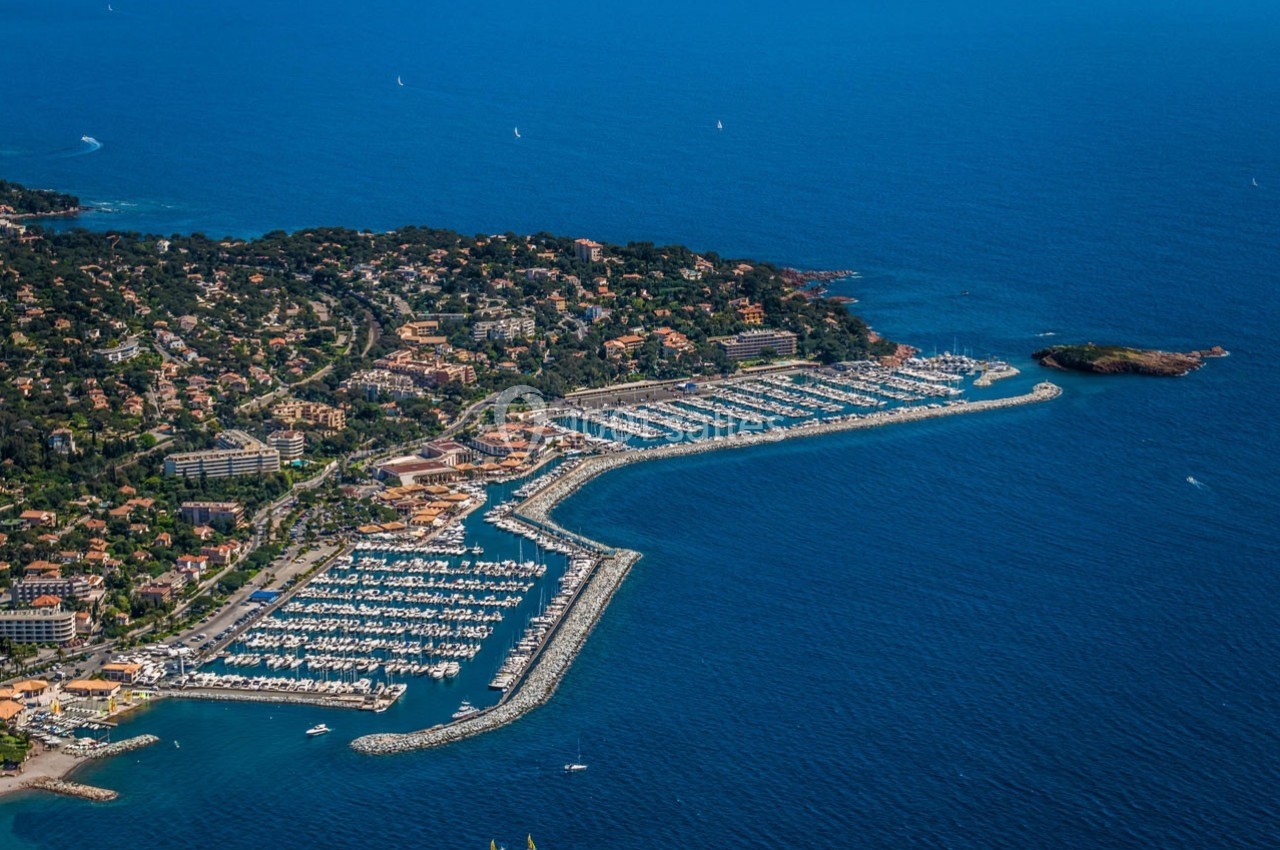 Vue aérienne d'un port de plaisance entouré de bâtiments résidentiels et de végétation, bordé par la mer.