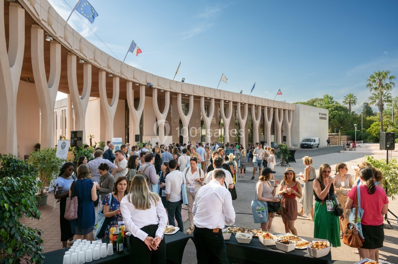 Groupe de personnes rassemblées lors d'un événement en extérieur devant un bâtiment moderne avec des drapeaux.