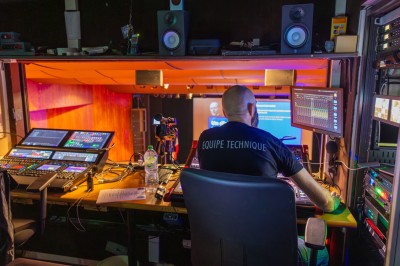 Une chanteuse en robe dorée se produit sur scène, entourée d'un chœur en tenues assorties, sous un éclairage bleu.