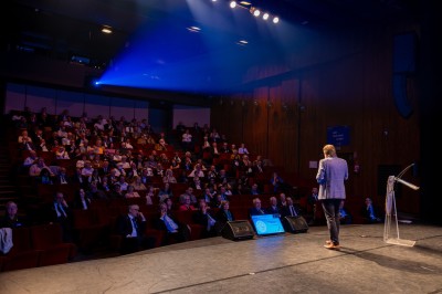 Une chanteuse en robe dorée se produit sur scène, entourée d'un chœur en tenues assorties, sous un éclairage bleu.