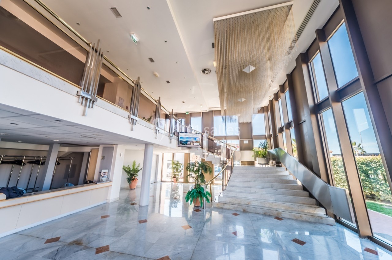 Hall spacieux avec escalier en marbre, grandes baies vitrées, plantes décoratives et lustre suspendu.