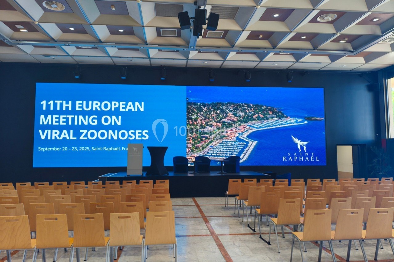 Salle de conférence vide avec écran affichant un événement sur les zoonoses virales à Saint-Raphaël, France.