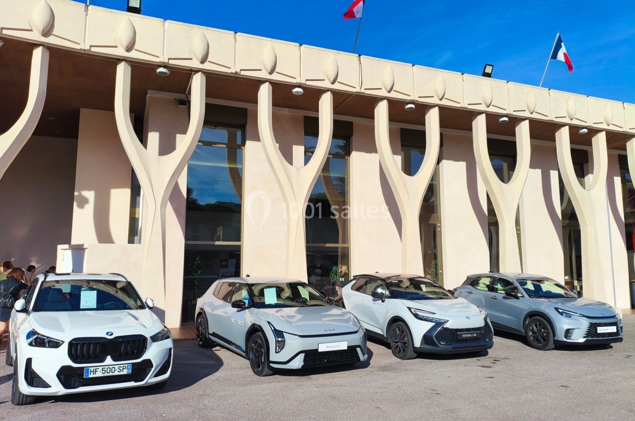 Quatre voitures électriques modernes stationnées devant un bâtiment beige avec des drapeaux français sur le toit.