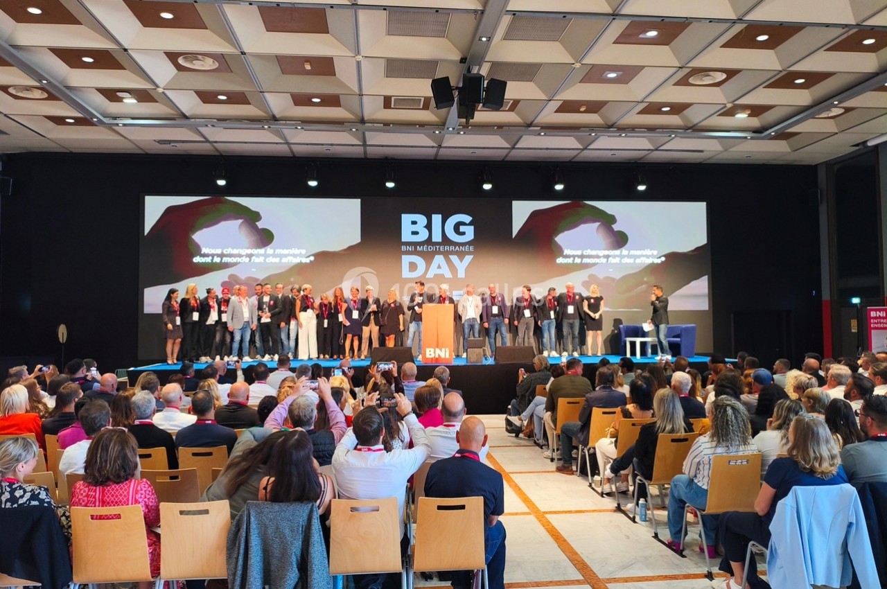 Des personnes sur une scène lors d'un événement professionnel, face à un public dans une grande salle.