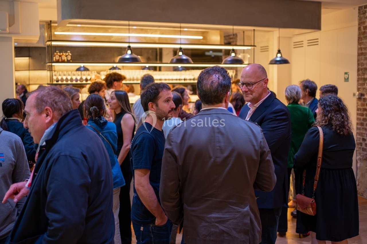 Groupe de personnes discutant dans un espace intérieur éclairé, avec un bar en arrière-plan.