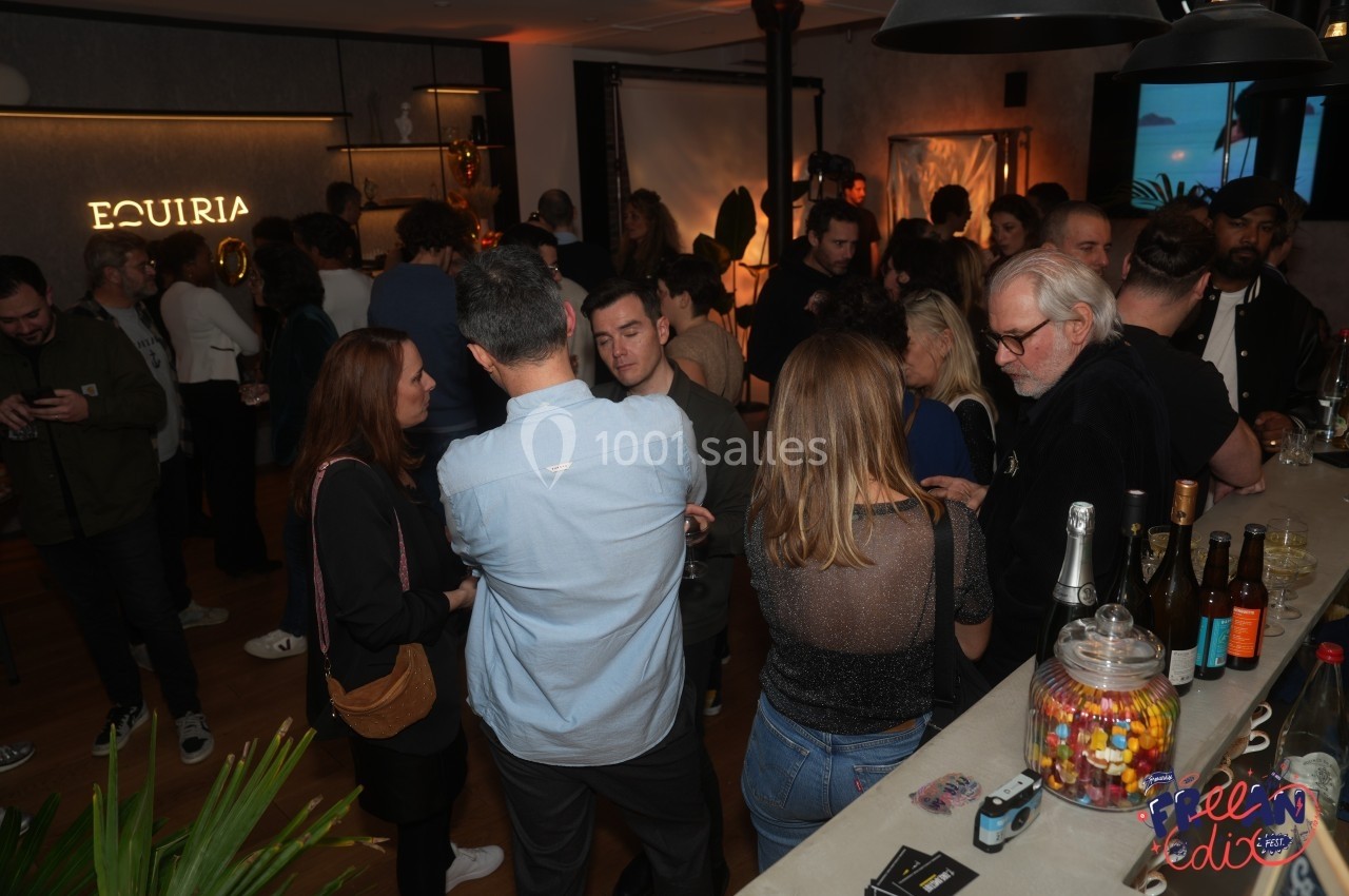 Groupe de personnes échangeant dans un espace intérieur lors d'un événement convivial, avec un bar au premier plan.