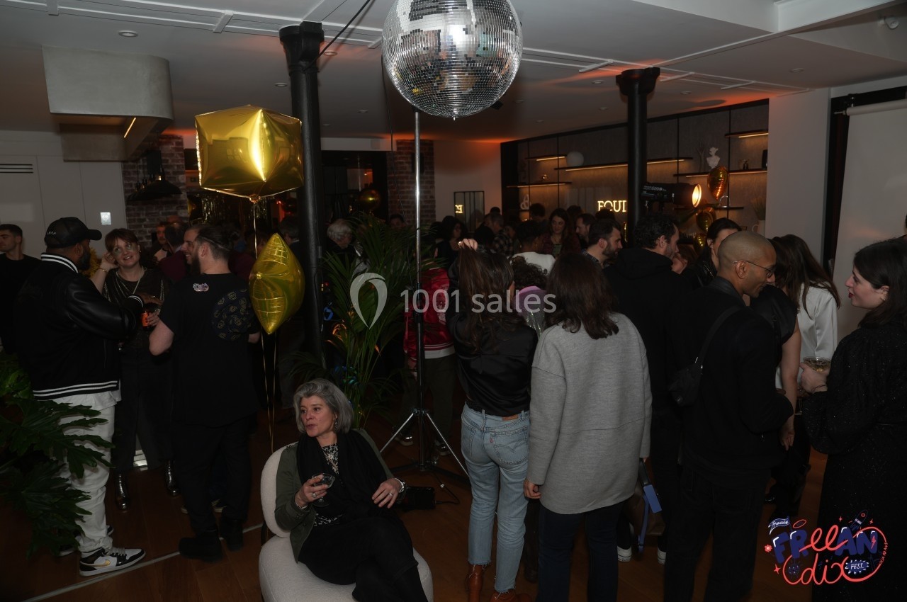 Groupe de personnes réunies dans un espace intérieur décoré avec des ballons dorés et une boule à facettes.