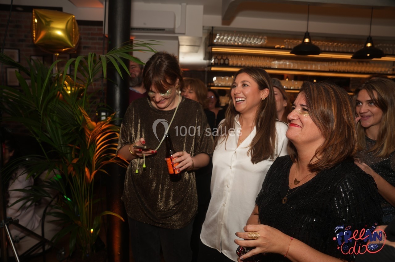 Des personnes souriantes participent à un événement festif dans un espace intérieur décoré de plantes et de ballons dorés.