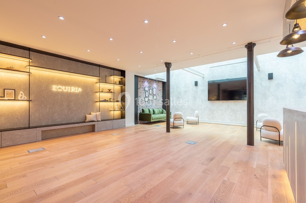 Salle lumineuse avec parquet en bois clair, étagères éclairées, canapé vert et écran mural dans un espace moderne.